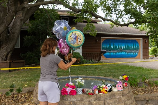 A woman places balloons on a memorial with candles, flowers and stuffed animals.