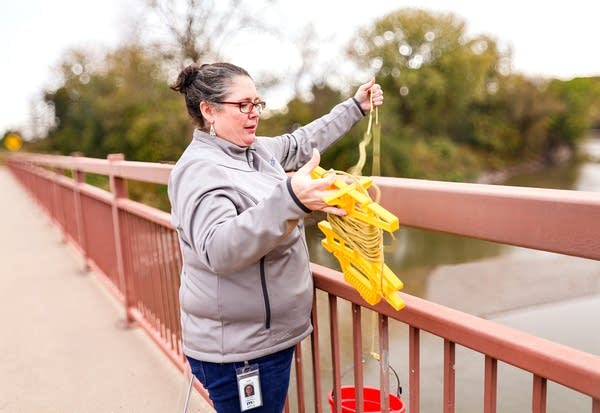 A woman on a bridge holds up yellow plastic water sample containers.