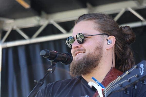 Close-up of a man in sunglasses playing guitar on stage.