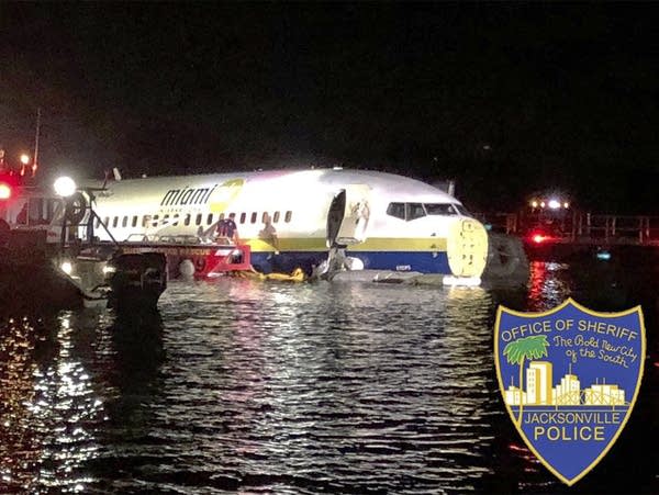 Authorities work at the scene where a plane slid into a river