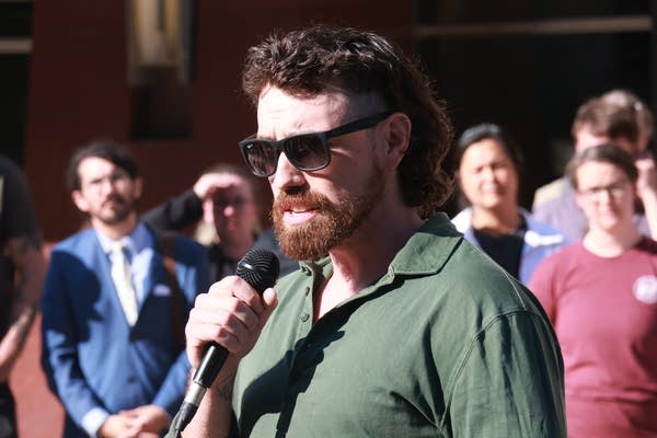man with beard & sunglasses speaks at rally