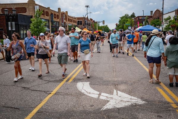 Crowds of people walk down a street during a summertime festival 