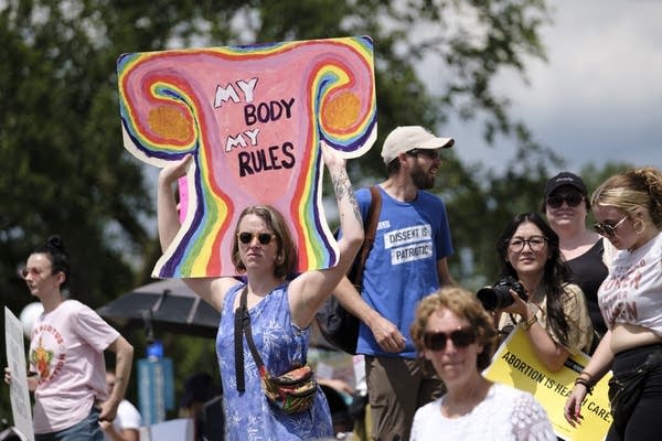 People hold signs and yell during a rally outside.