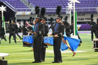 A marching band performs on the field of a football stadium.