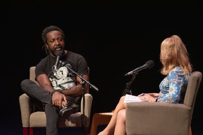 Two people sit on a stage with microphones.