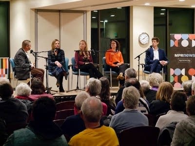 Five people sit on a stage in front of an audience.