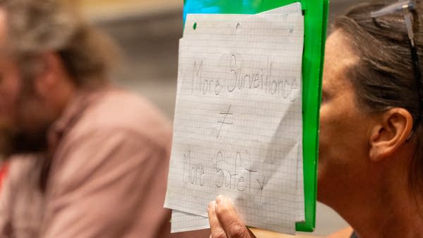 A woman holds a sign that reads 'More surveillance does not equal more safety.