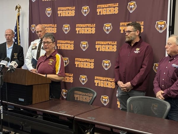 A woman speaks at a podium in front of a banner with "Stewartville Tigers" iconography.