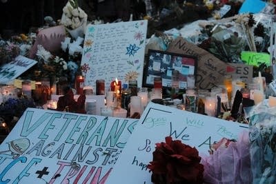 A group of people gather around a memorial full of signs, flowers and candles.