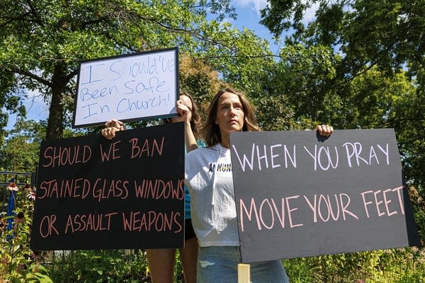 Two women hold protest signs. One reads, "When you pray, move your feet."