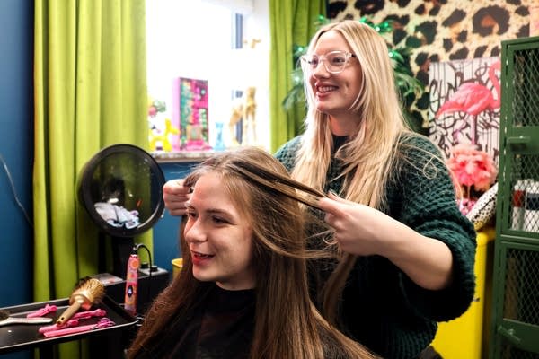 A stylist plays with her client's hair while they speak.