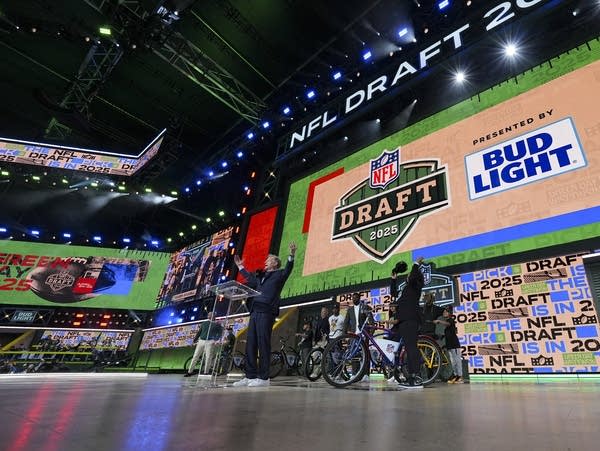 A man on a stage raises his hands