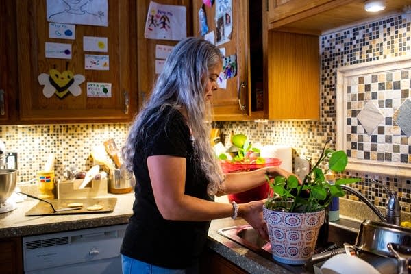 A person stands next to the sink with potted plants on the counter.