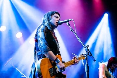 A musician sings and plays guitar onstage in a music venue
