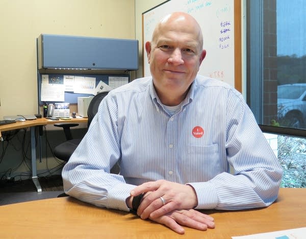 A man wearing a blue shirt poses for a picture at a desk. 