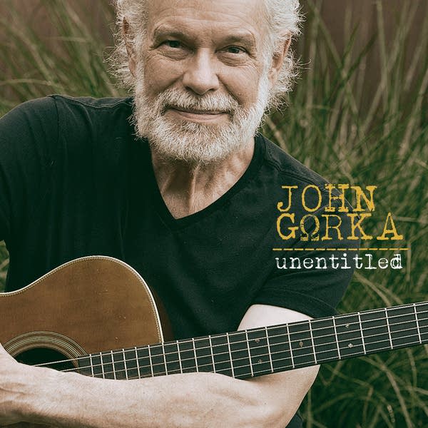 A man holding a guitar poses for a portrait among tall grass
