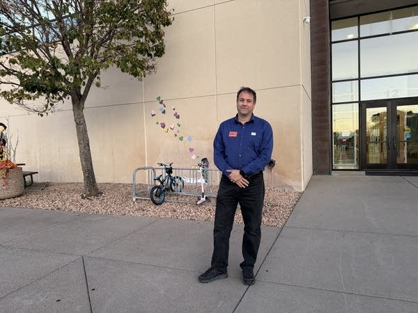 A man stands outside of a building with his hand crossed in front of him.