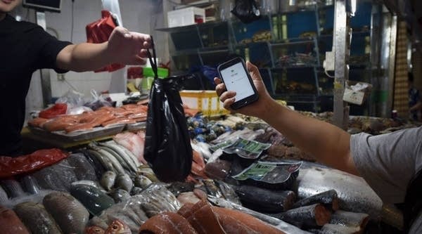 A man making purchases through his smartphone at a seafood booth at a market in Beijing, June 2017.
