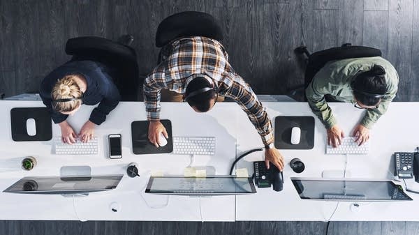 An overhead shot of three tech workers working on computers.