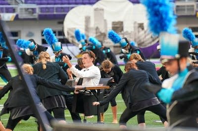 A marching band performs on the field of a football stadium.
