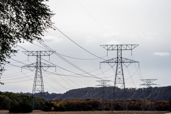 Power lines arc across the sky in front of autumn foliage.