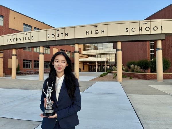 A woman holding a trophy standing in front of a high school