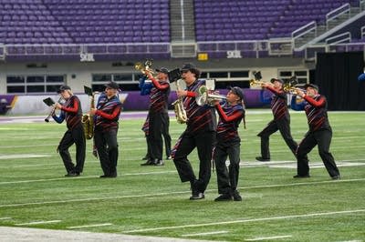 A marching band performs on the field of a football stadium.