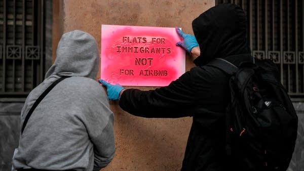 Activists stencil a slogan reading "Flats for immigrants not for airbnb" on a wall during a demonstration outside the EU offices in central Athens on April 16, 2019 to ask for funding for the EU ESTIA emergency support package which provides urban accommodation and cash assistance to refugees and asylum-seekers in Greece. 