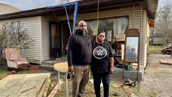 Kevin and Gwendolyn Comeaux stand in front of a house damaged by the 2024 Houston derecho.