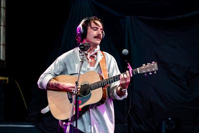 A musician sings and plays guitar on an outdoor stage