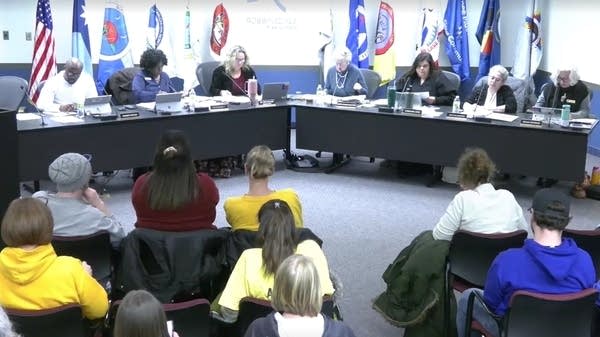 A school board meets with a large crowd in attendance