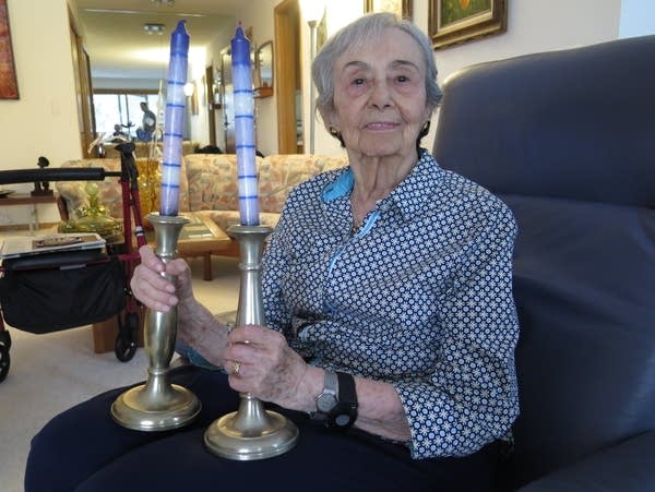 A woman holds two candlesticks. 