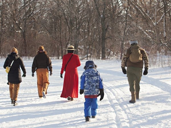 Five people walk on a snowy trail