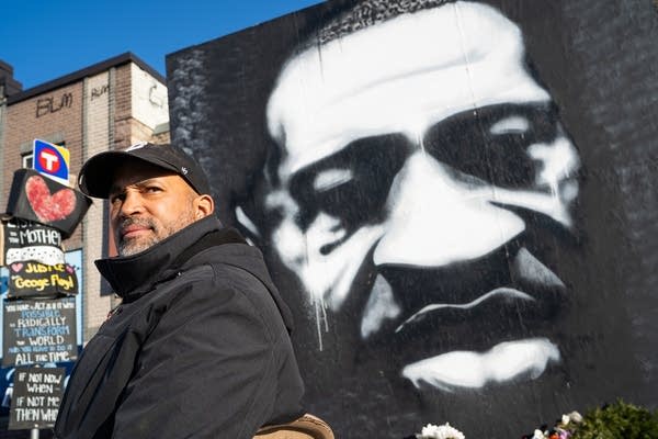 A man sits in front of a large black and white painting.