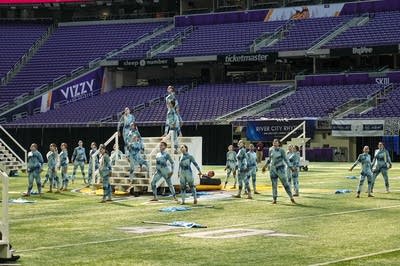 A marching band performs on the field of a football stadium.