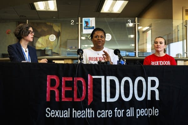 Three people sit and address the media