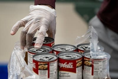 A%20gloved%20hand%20picks%20up%20a%20can%20of%20soup.