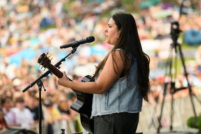 A musician sings and plays guitar on a large outdoor stage