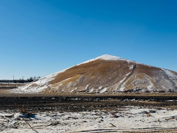 A large pile sits in a field, lightly covered in spots with snow.