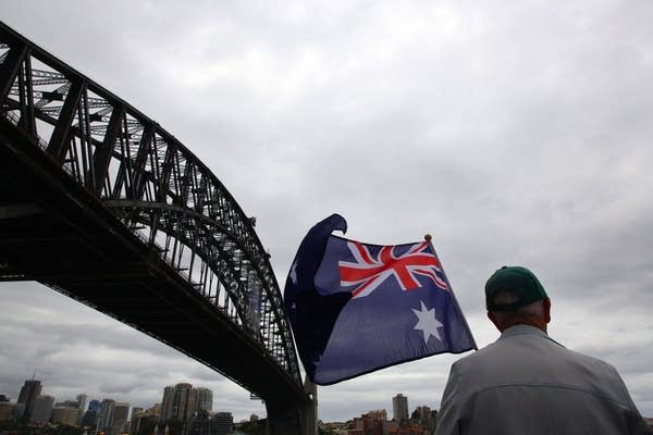 2014 Australia Day celebrations on Sydney Harbour foreshore. Spectators wave flags as a procession of boats pass under the Sydney Harbour Bridge.