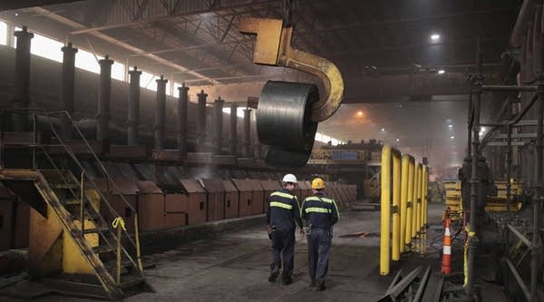 Workers remove a coil from the production line for quality-control testing during steel production at the NLMK Indiana steel mill in March in Portage, Indiana.