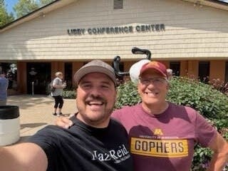 A man and his son pose smiling for a selfie in front of a beige building that reads "Libby Conference Center."
