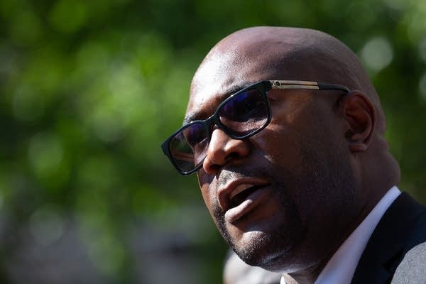 A man in sunglasses speaks at a press conference.