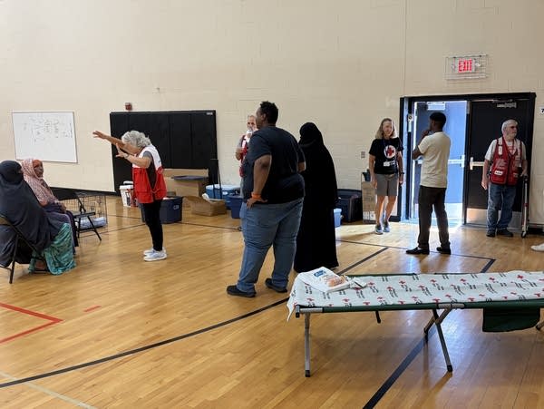 Volunteers in red vests speak to a family inside a school gymnasium.