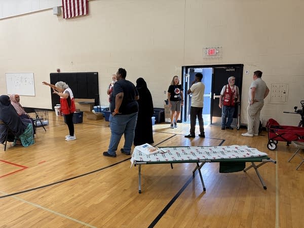 Volunteers in red vests speak to a family inside a school gymnasium.