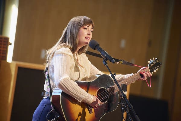 A musician sings and plays guitar in a small auditorium