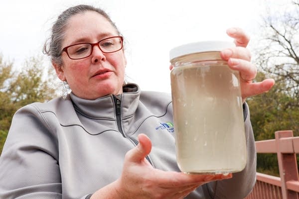 A woman holds up a jar of cloudy water to the camera.