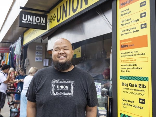 A Hmong man stands in front of a state fair booth