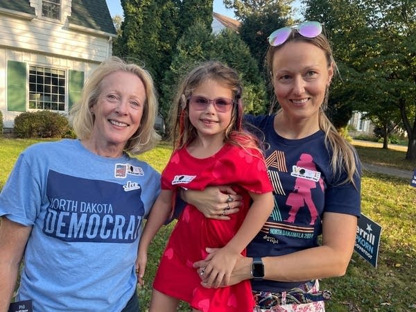 Three people pose outside of a house.