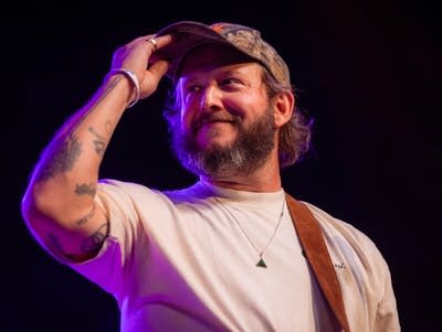 Justin Vernon holds the brim of his cap.